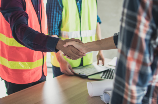 作業着姿で握手をする男性